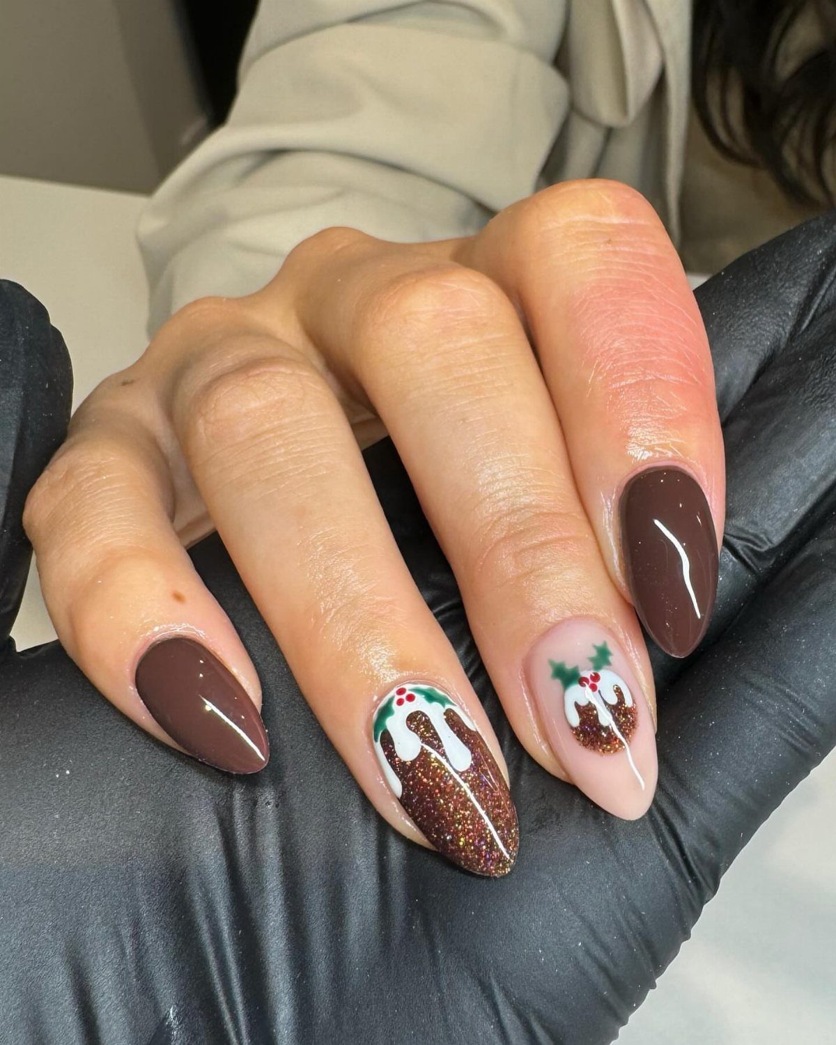 Almond-shaped nails featuring dark brown polish and Christmas pudding nail art with white icing.