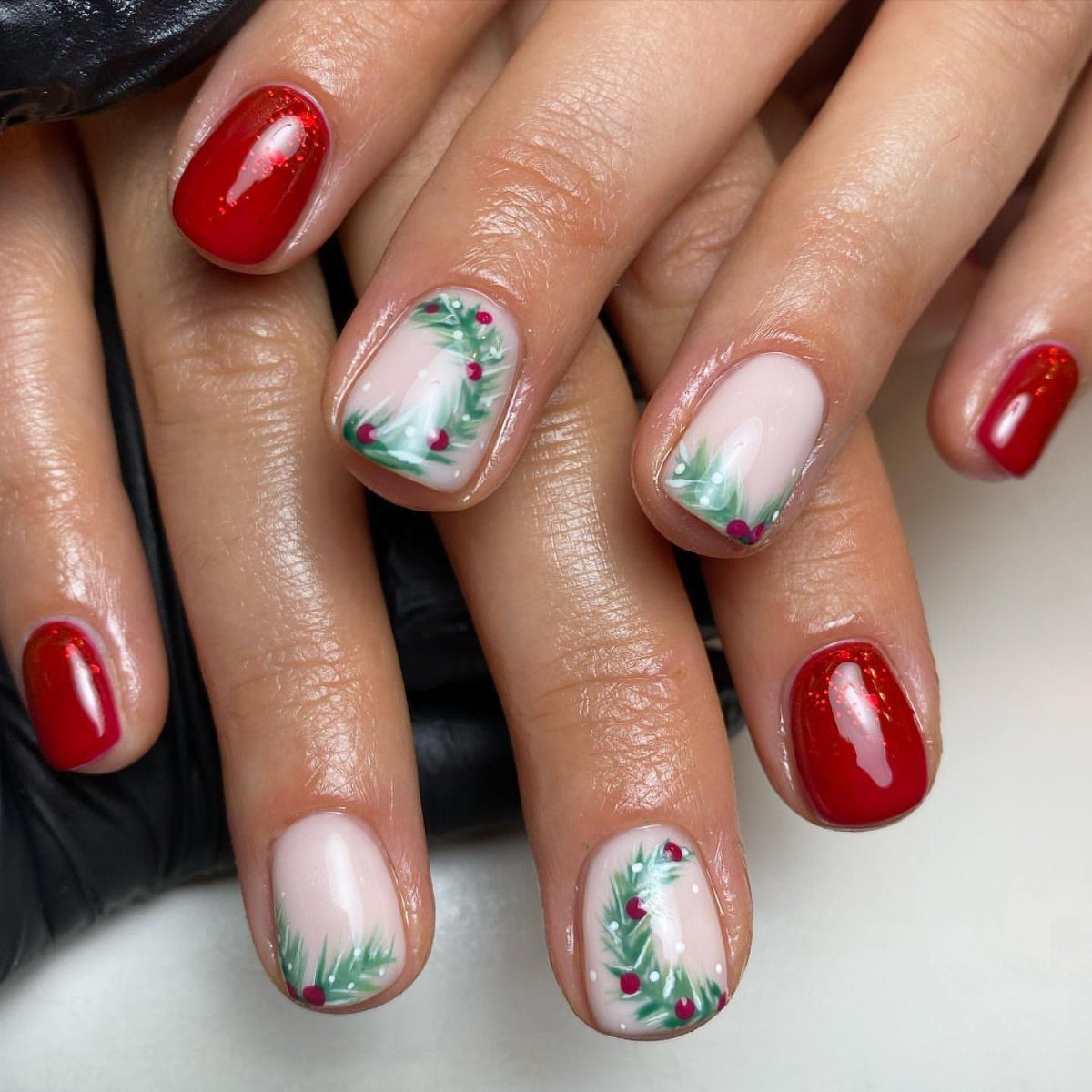 Manicured nails featuring glossy red polish and pale pink nails with green wreath art.