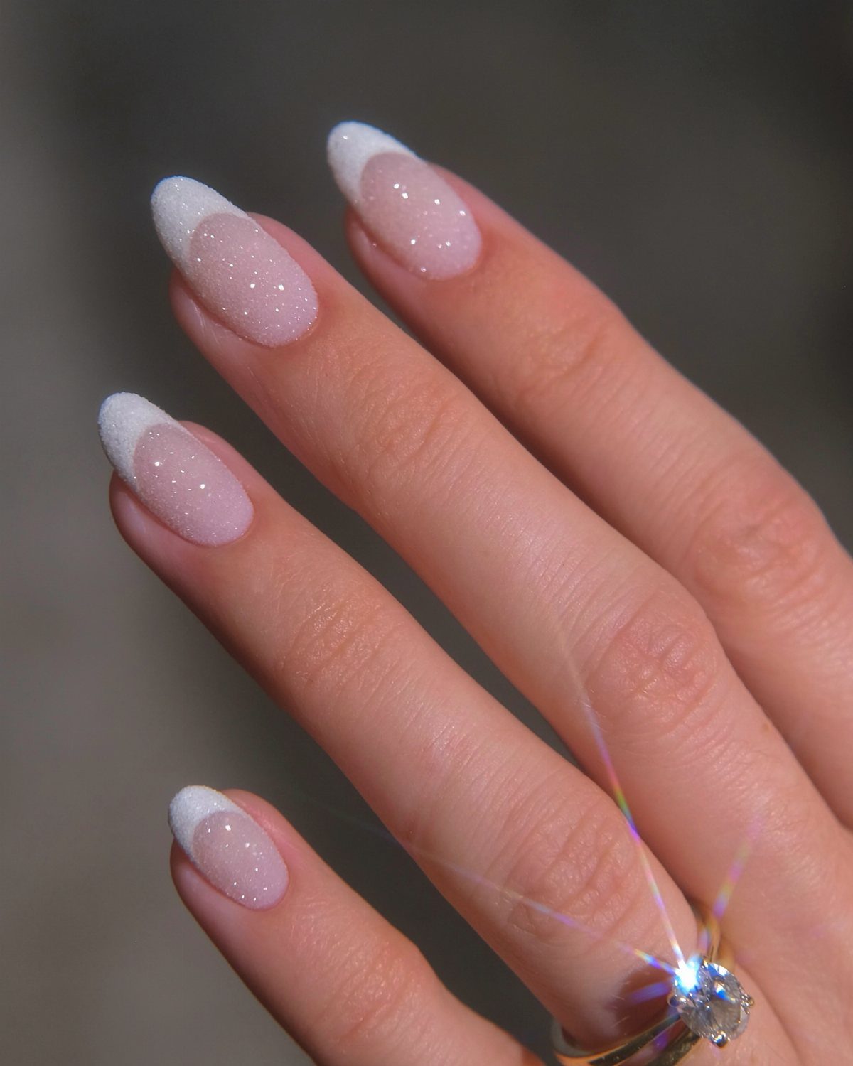 Oval nails with shimmering pink glitter and classic white French tips and a diamond ring
