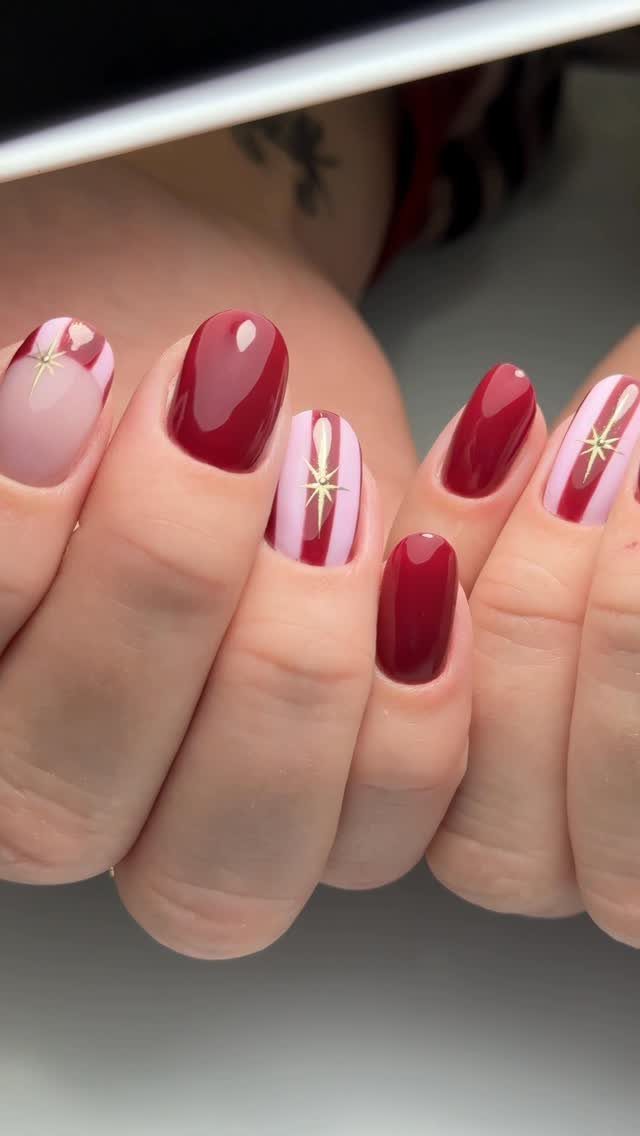 Manicured nails with deep red polish, pink stripes, and gold star accents.