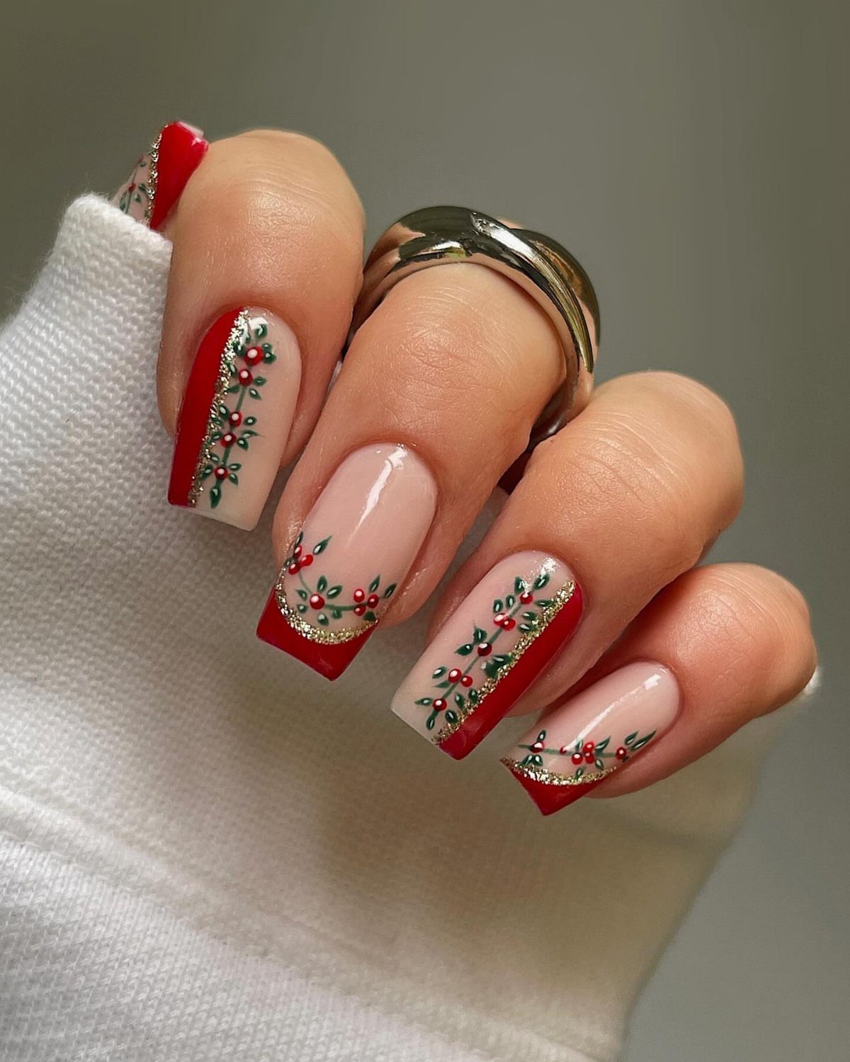 Manicured nails with red and nude polish featuring painted holly berry designs.