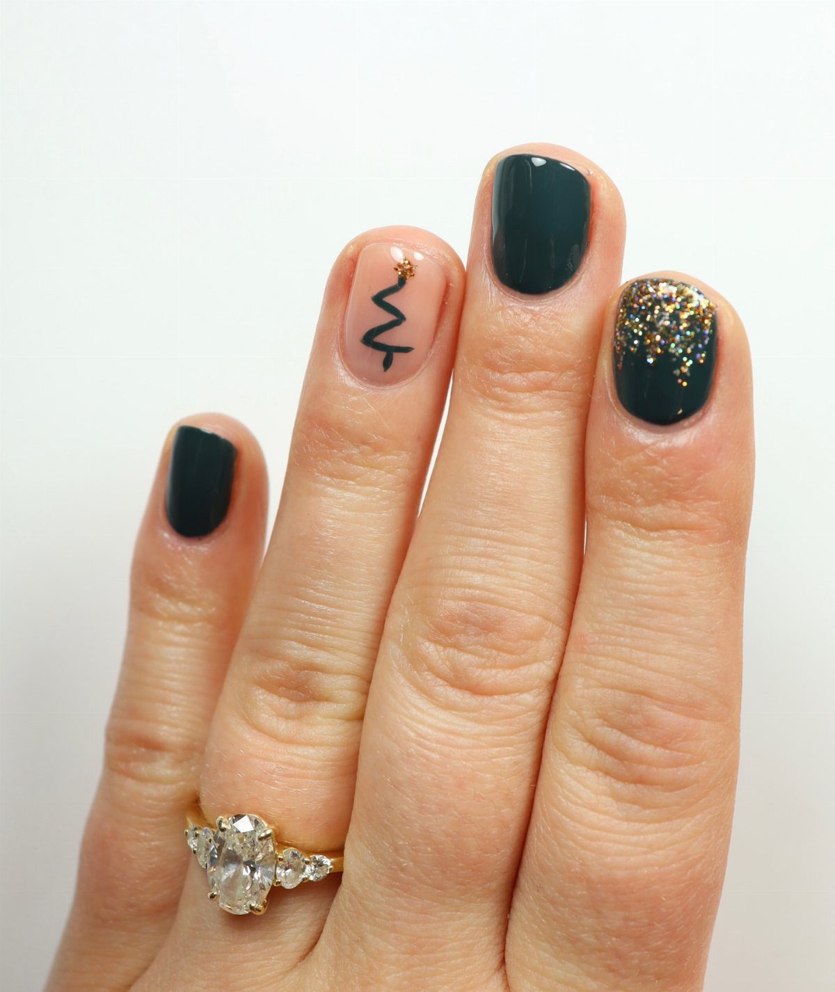 Manicured nails featuring dark green polish and a minimalist Christmas tree accent nail.