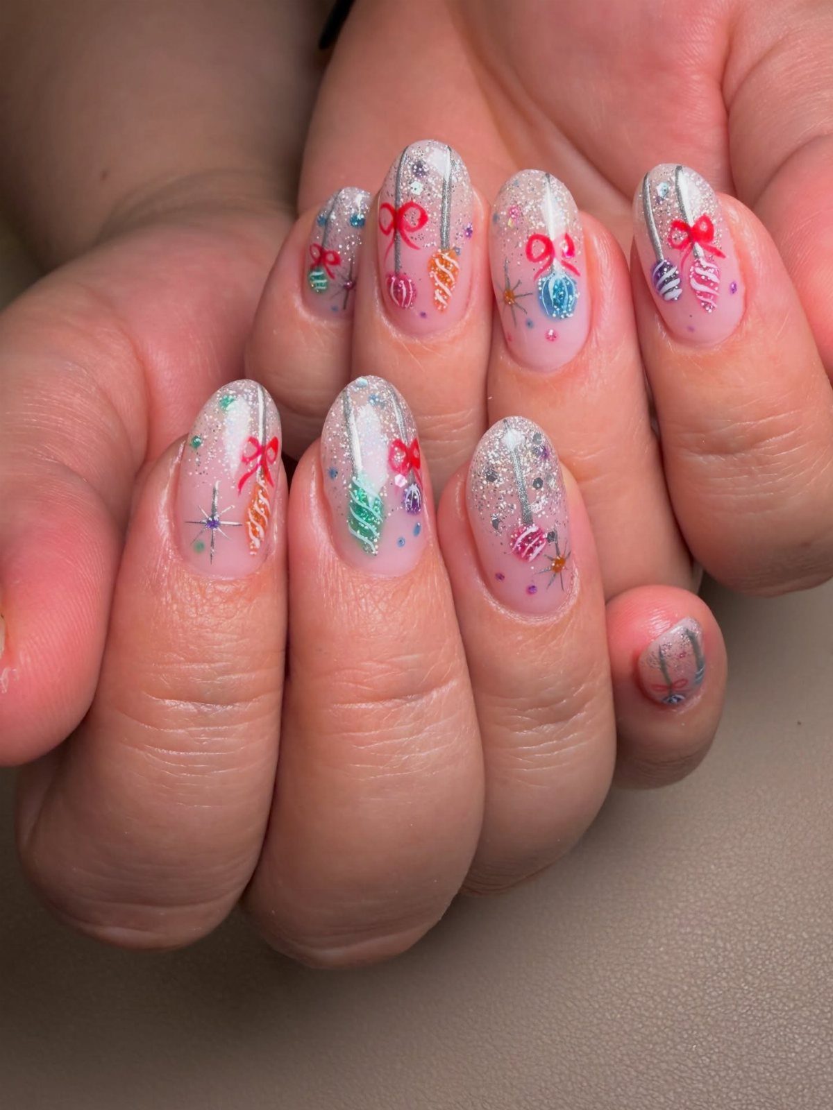 Fingernails with clear polish and silver glitter featuring various colorful Christmas ornament designs.