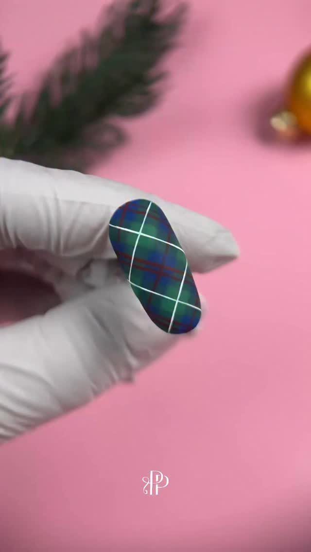 Plaid patterned artificial nail held by a gloved hand against pink background