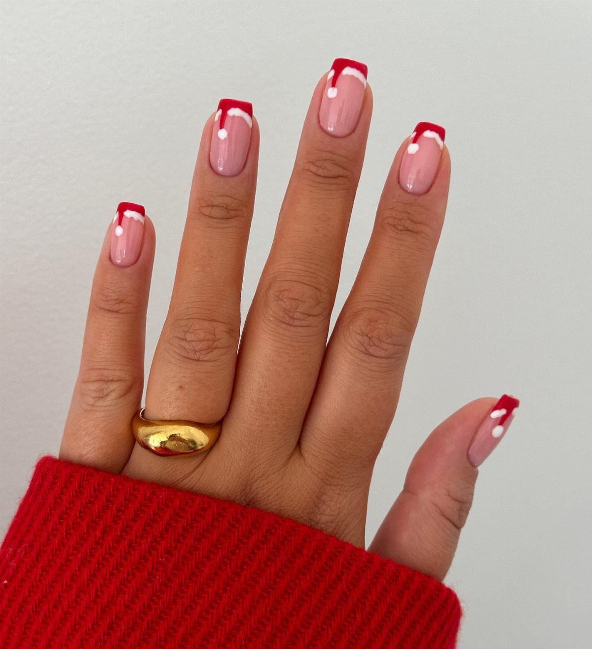 Nails with red French tips designed to look like Santa hats with white pom-poms.