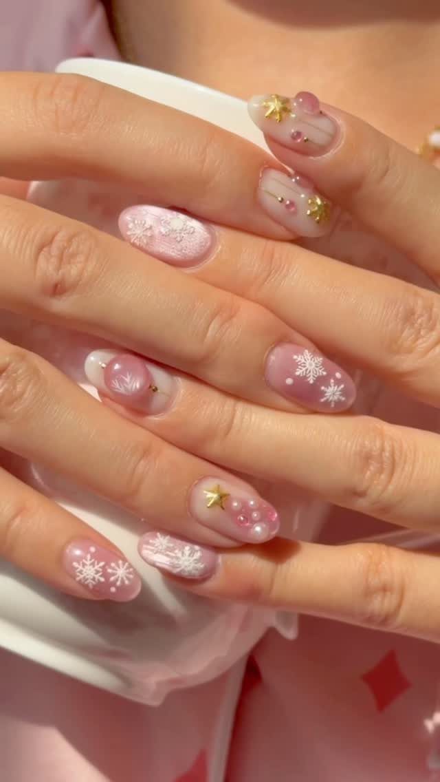 Manicured nails with pink polish, gold stars, and white snowflake designs.