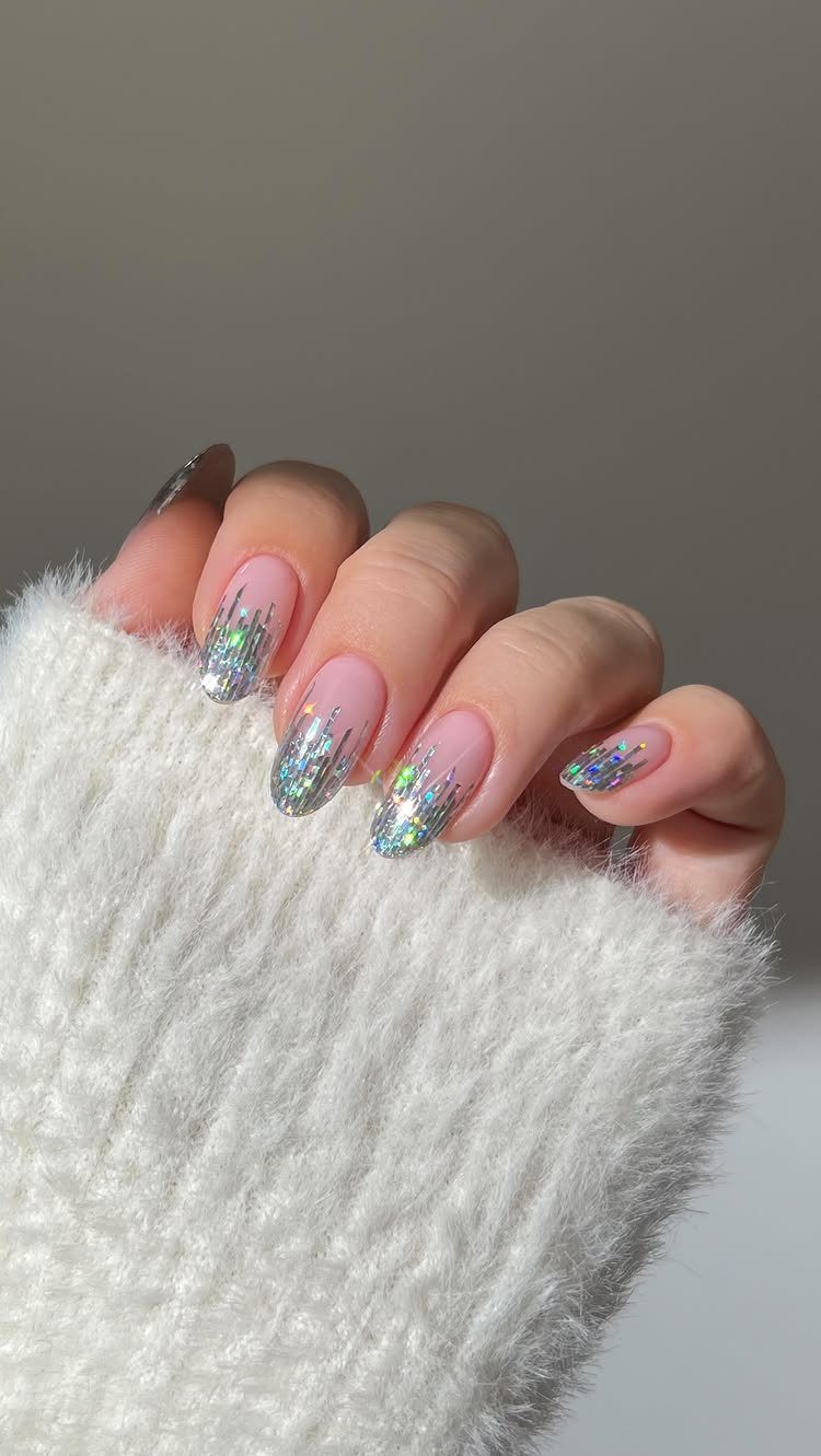 Manicured nails with iridescent holographic glitter tips and a white fuzzy sweater sleeve.