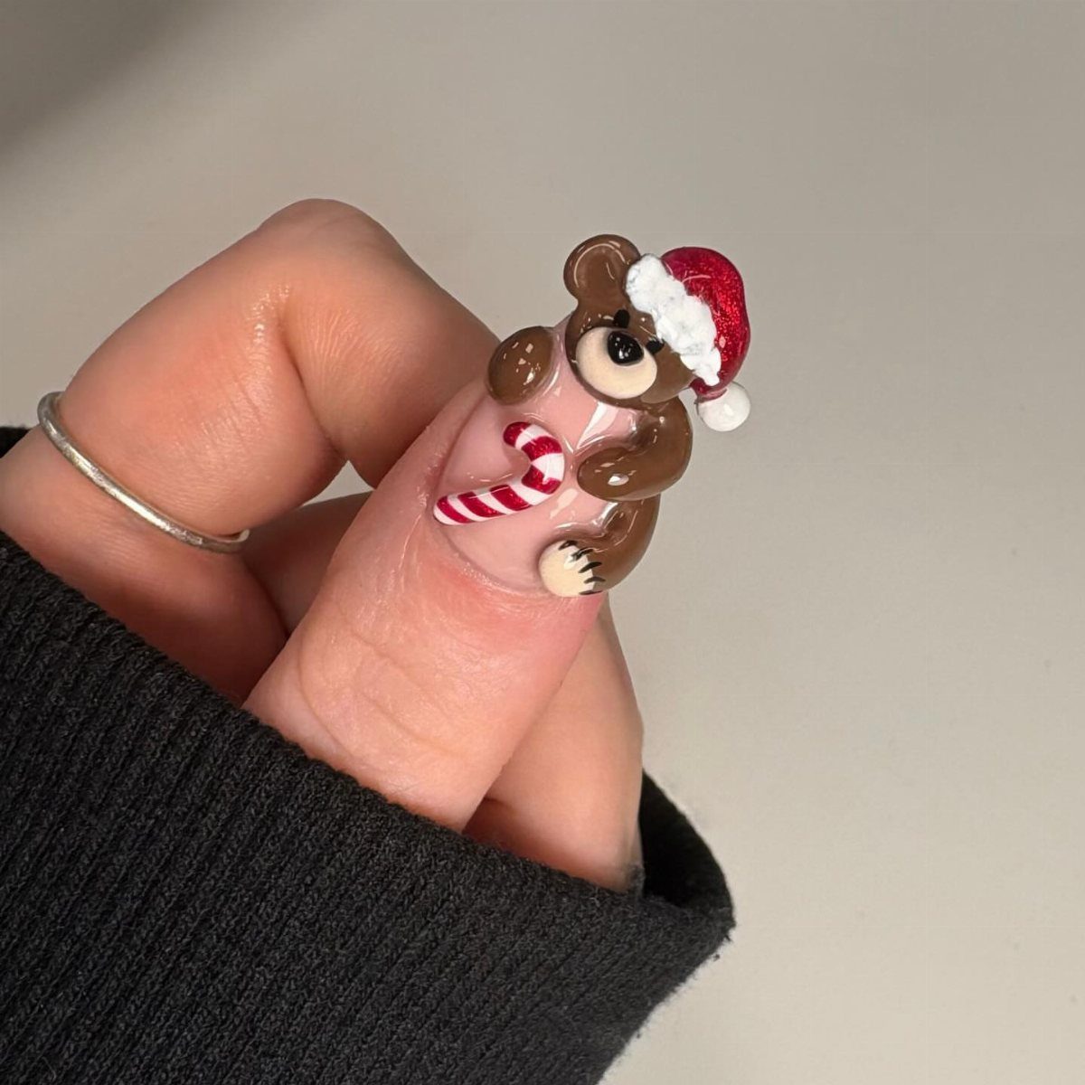 3D nail art of a brown bear in a Santa hat holding a candy cane