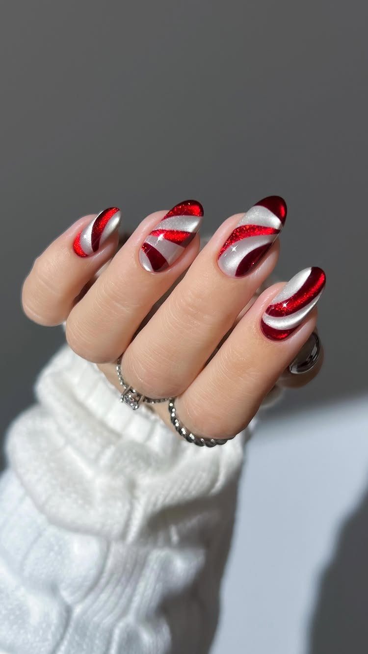 Almond-shaped nails with red and white swirling candy cane stripes and silver rings.