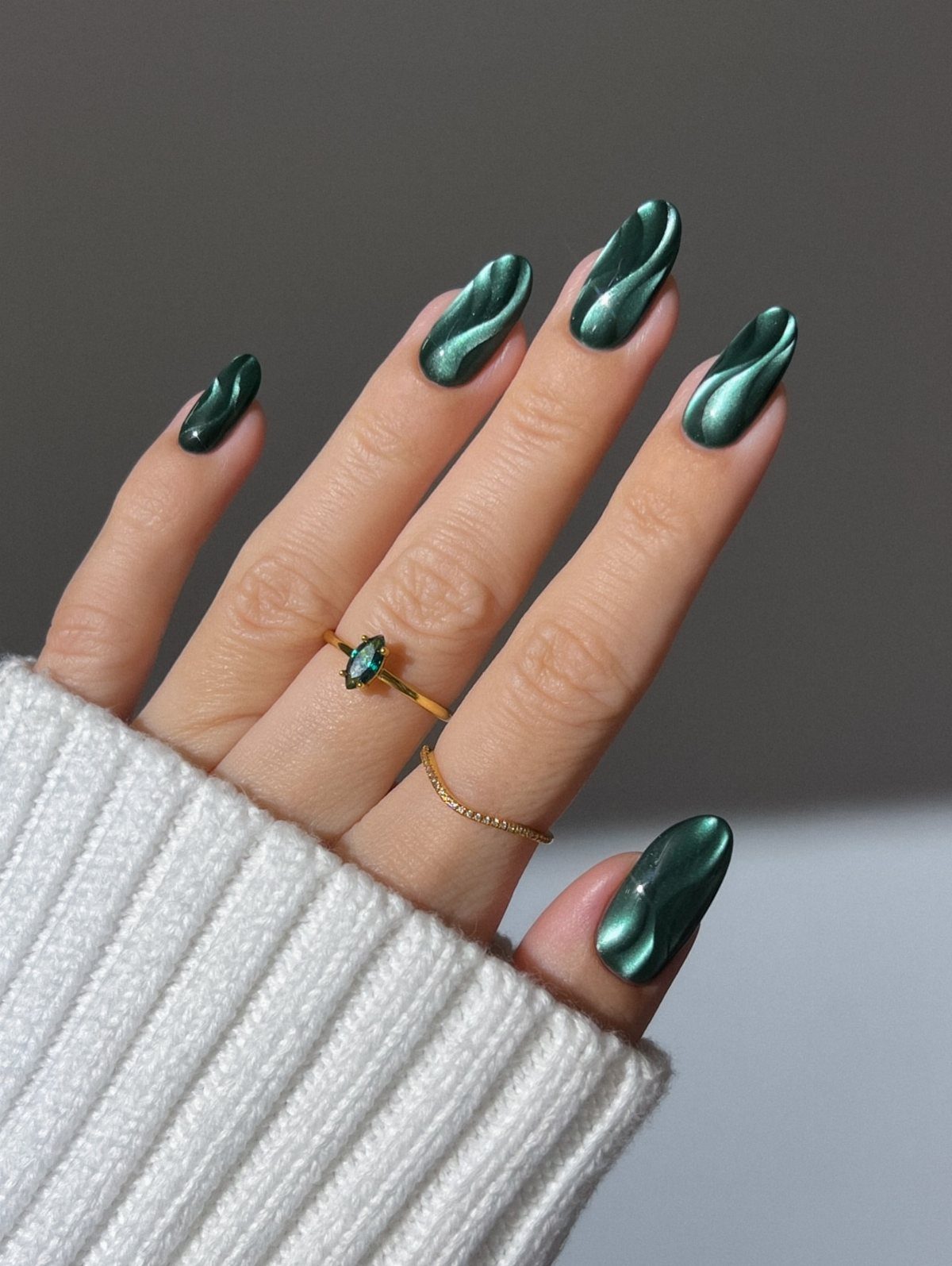 Dark green chrome nails with 3D swirls and gold rings on a hand.