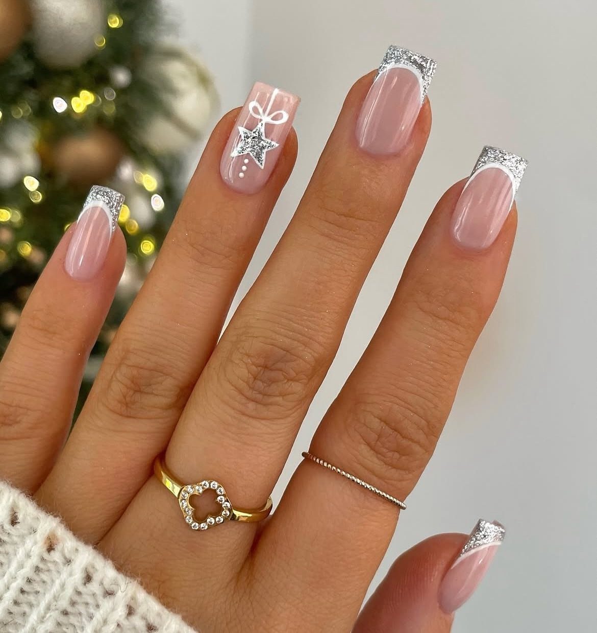 Manicured nails with silver glitter tips and a white bow accent nail.
