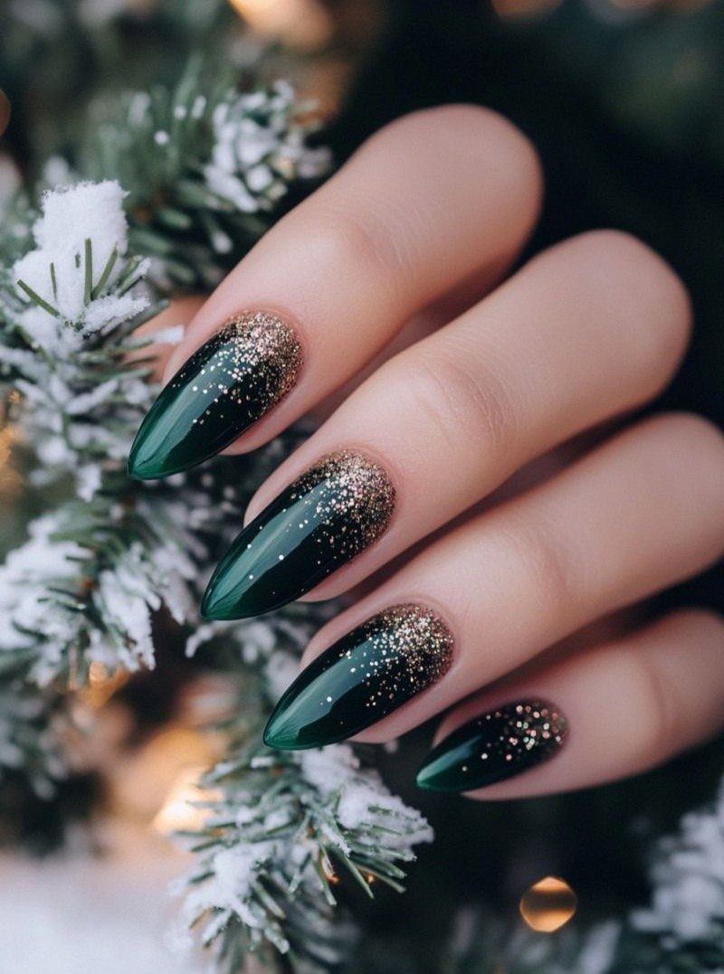 Deep green almond nails with gold glitter gradients resting on snowy pine branches.