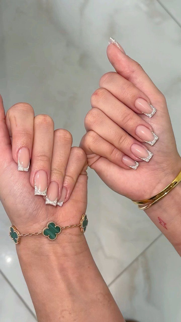 Nude almond nails with sparkling silver glitter French tips and gold jewelry.