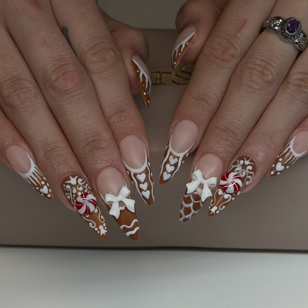 Almond-shaped nails with brown gingerbread icing designs, white bows, and peppermint candies.