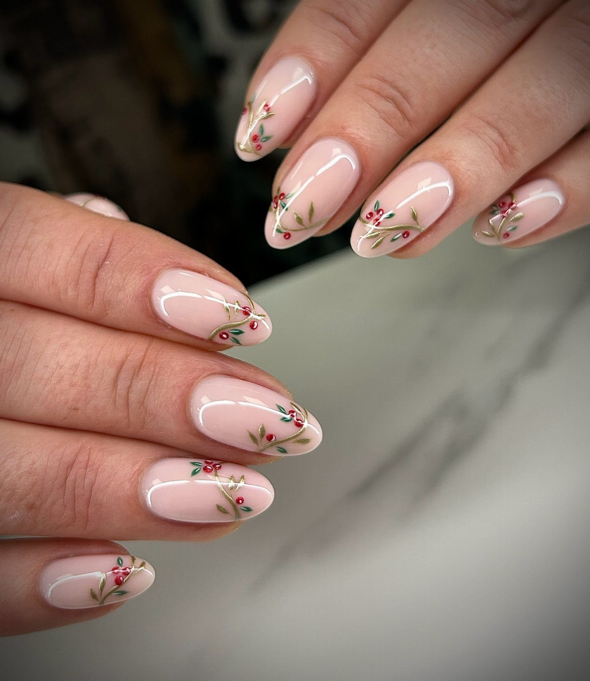 Nude oval nails decorated with small red berries and green leaves.