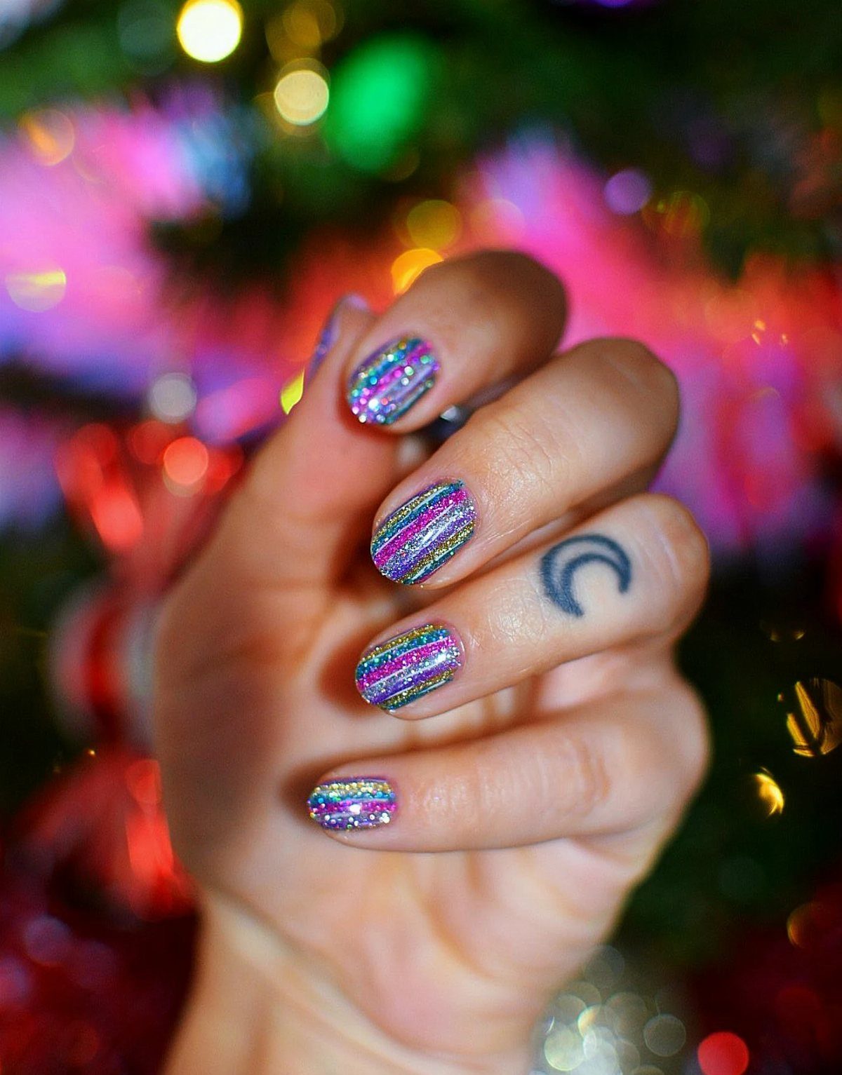 Holographic glitter nails on a hand against a blurred Christmas tree background