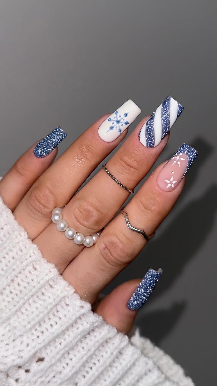 Winter themed nails with blue glitter, white snowflakes, and blue stripes on coffin nails.