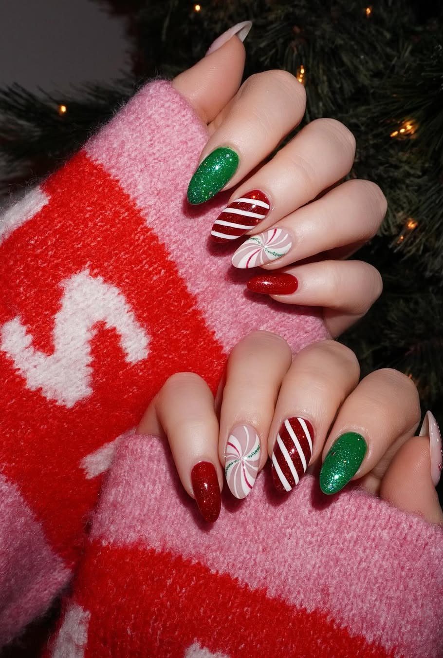 Almond-shaped nails with red, green, and white holiday designs and a knit sweater.