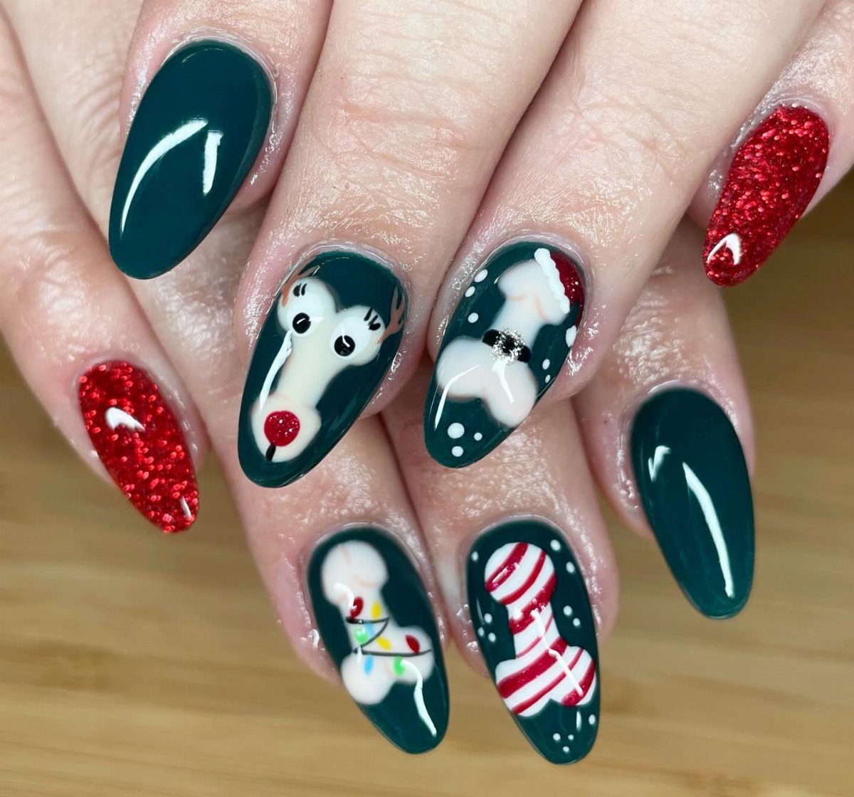 Almond-shaped nails with dark green polish and festive art including a reindeer face.