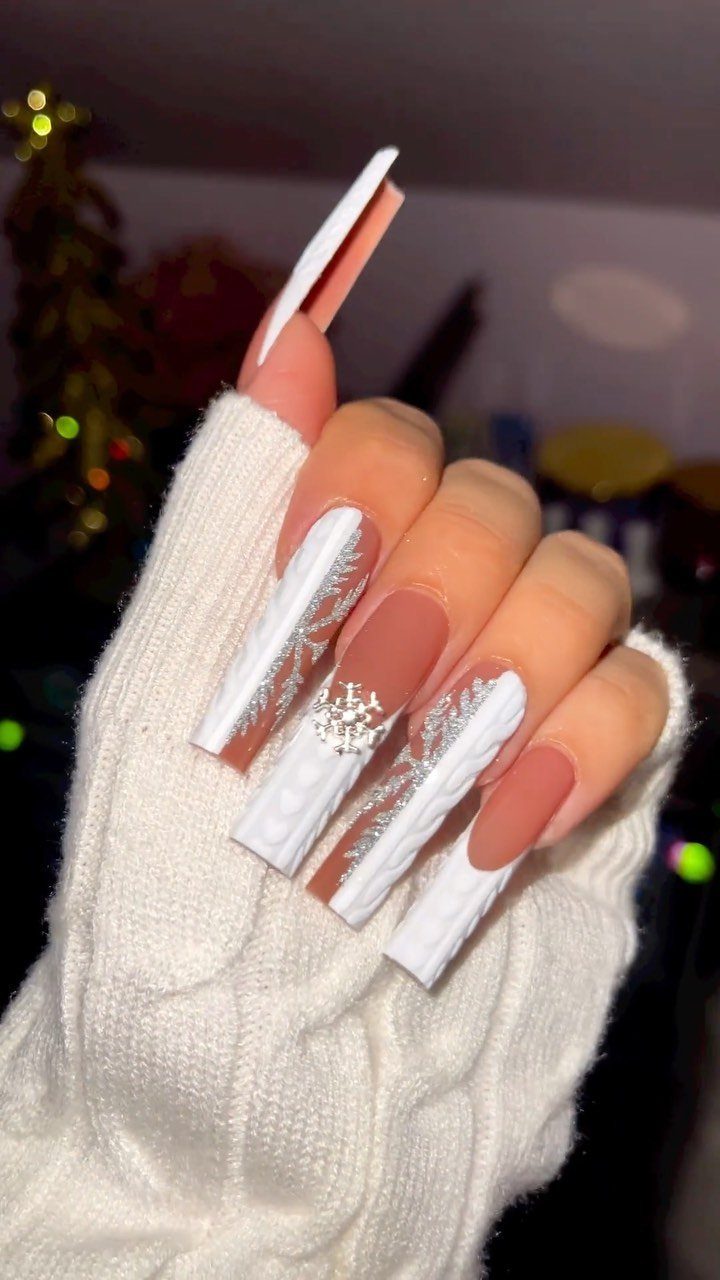 Long acrylic nails with white snowflake designs and matte brown polish on a sweater