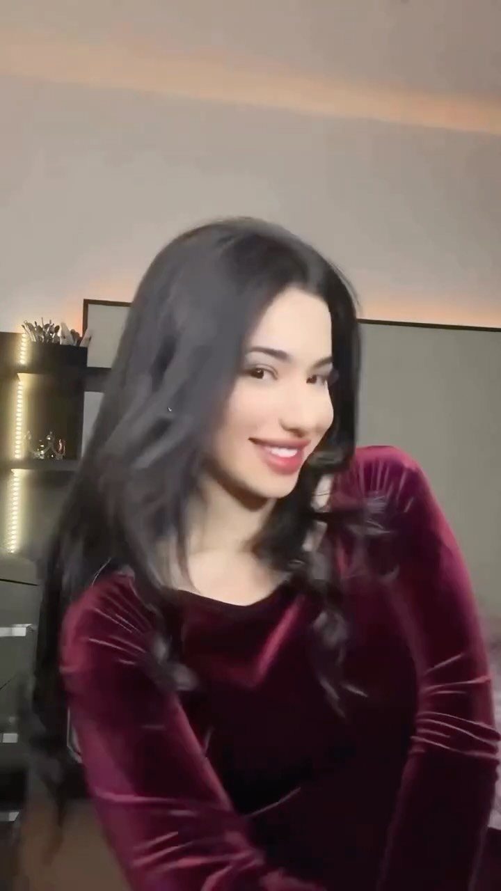 Young woman with long dark hair wearing a burgundy velvet dress and smiling.