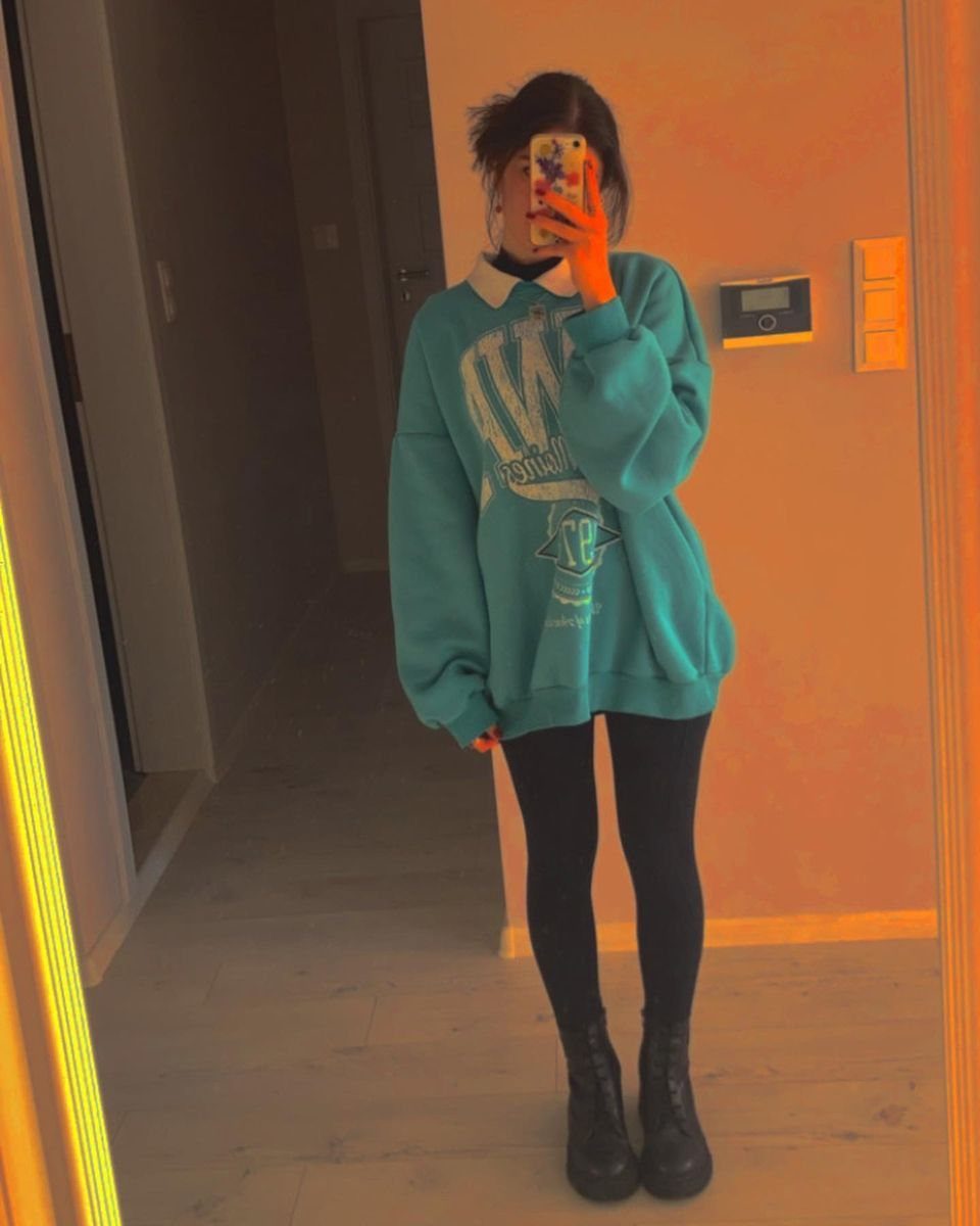 Person in oversized blue sweatshirt and black leggings taking a mirror selfie indoors.