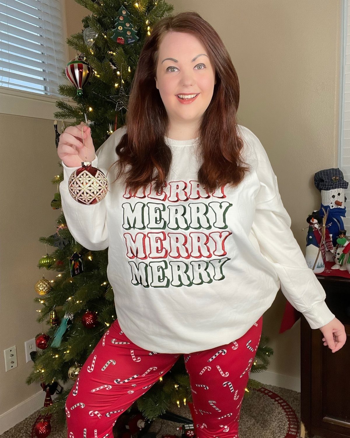 Woman in red candy cane pants and white merry sweatshirt by Christmas tree