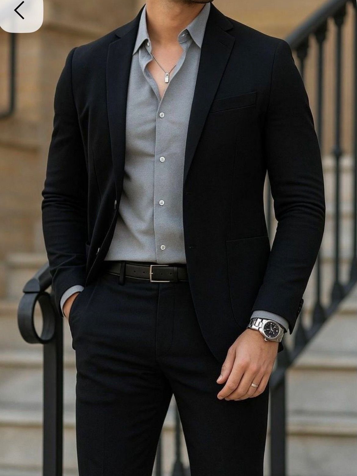 Man in a black tailored suit and grey shirt standing on stone steps.