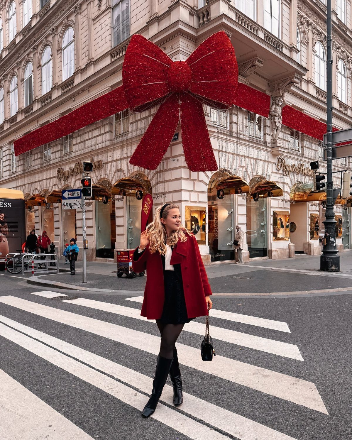 Woman in a red coat and black skirt standing before a giant red bow.