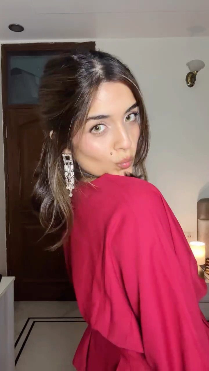 Woman in a bright red dress and sparkly earrings posing indoors.