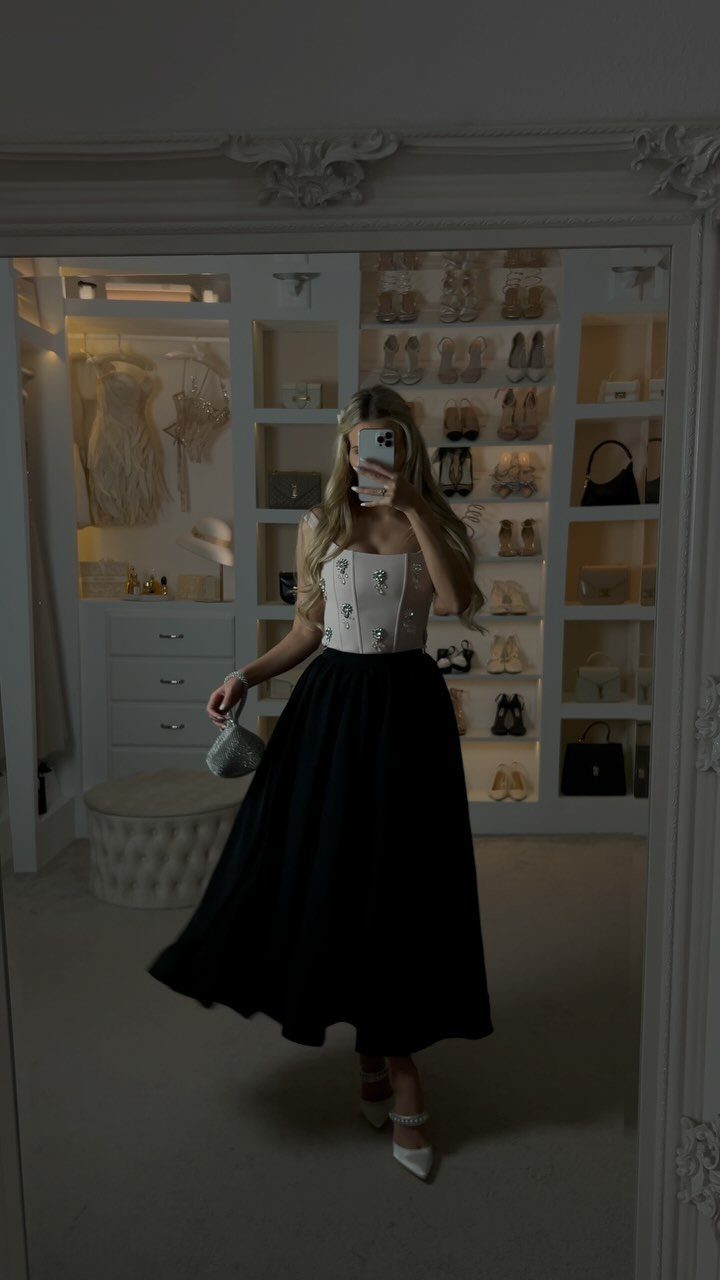 Woman in a white corset top and long black skirt posing in closet
