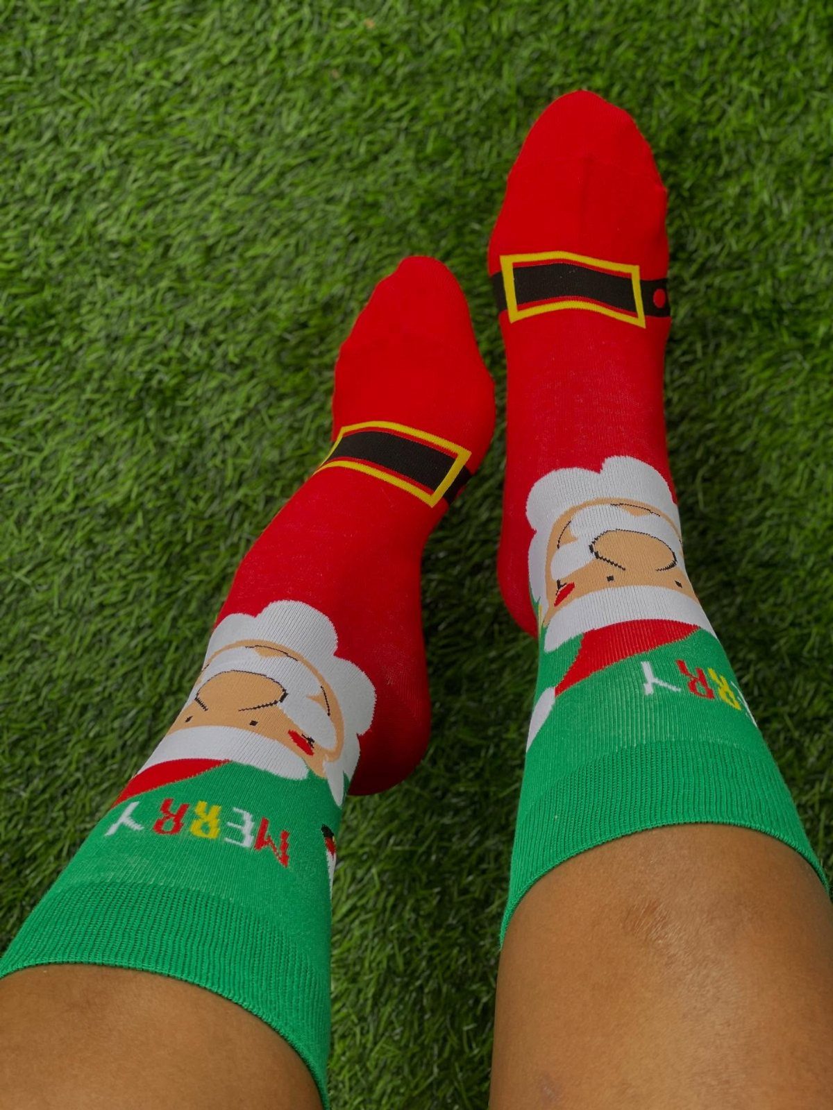 Christmas socks with Santa Claus patterns worn on feet over green grass
