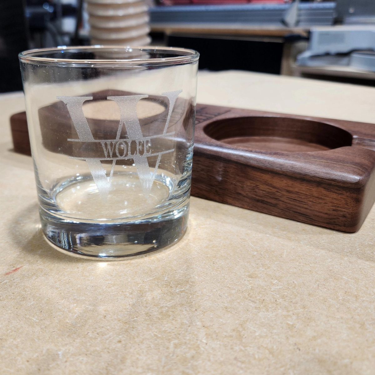 Etched whiskey glass and wooden cigar holder resting on a light beige surface.