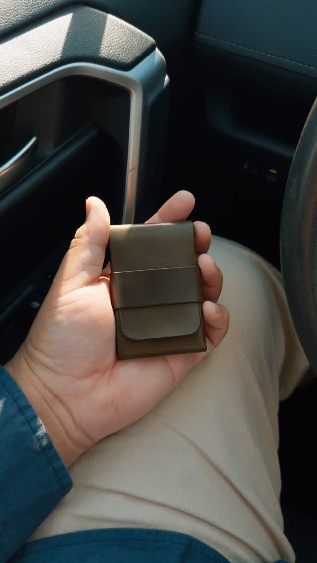 Brown leather wallet held in a hand inside a car interior