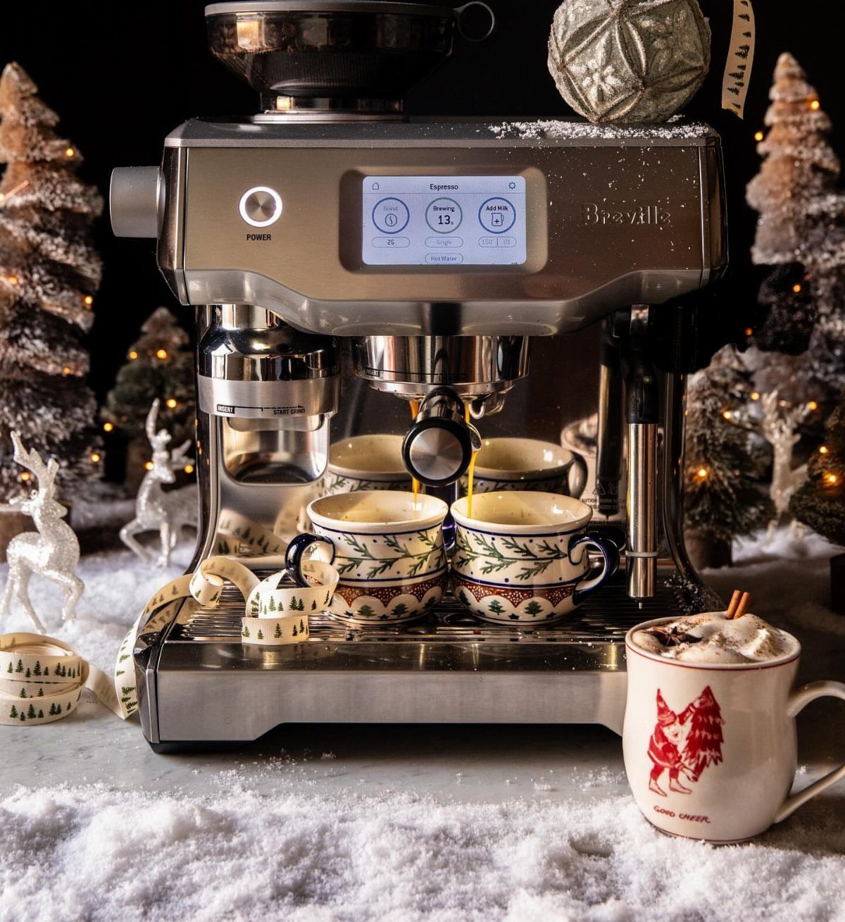 Silver espresso machine brewing coffee in a festive winter scene with snow and trees
