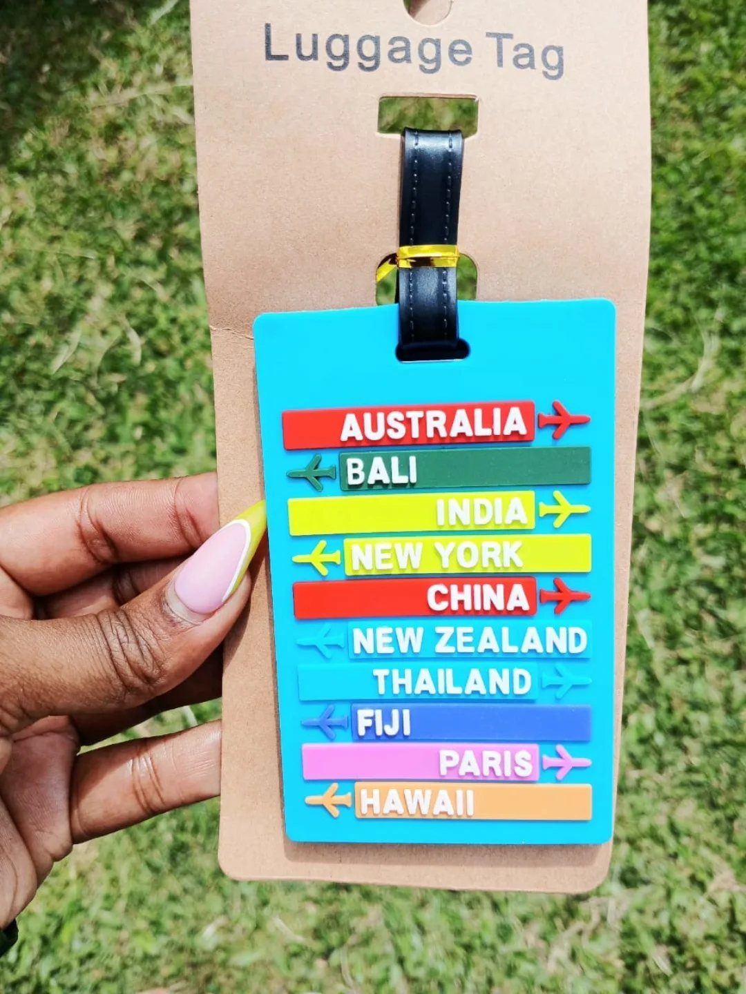 Blue luggage tag with colorful destination strips held against a grassy background