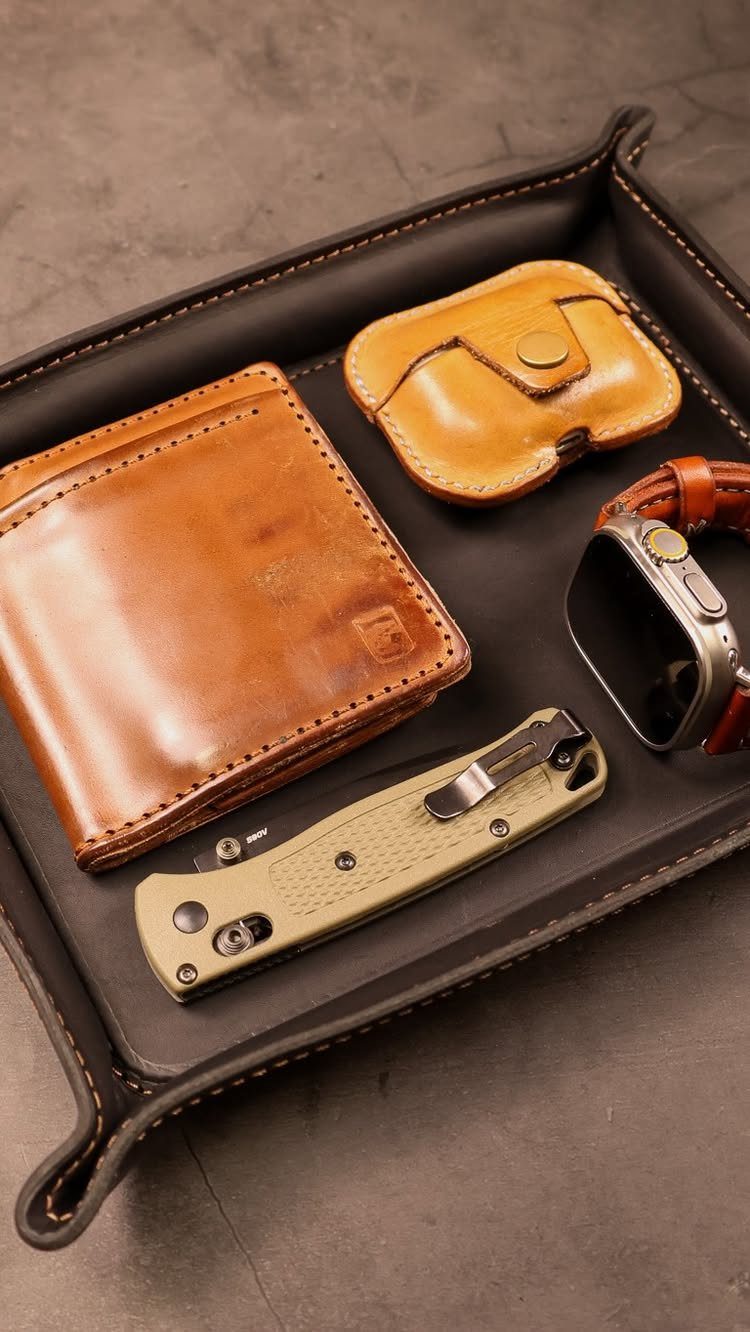 Leather valet tray with wallet, AirPods case, smartwatch, and pocket knife.
