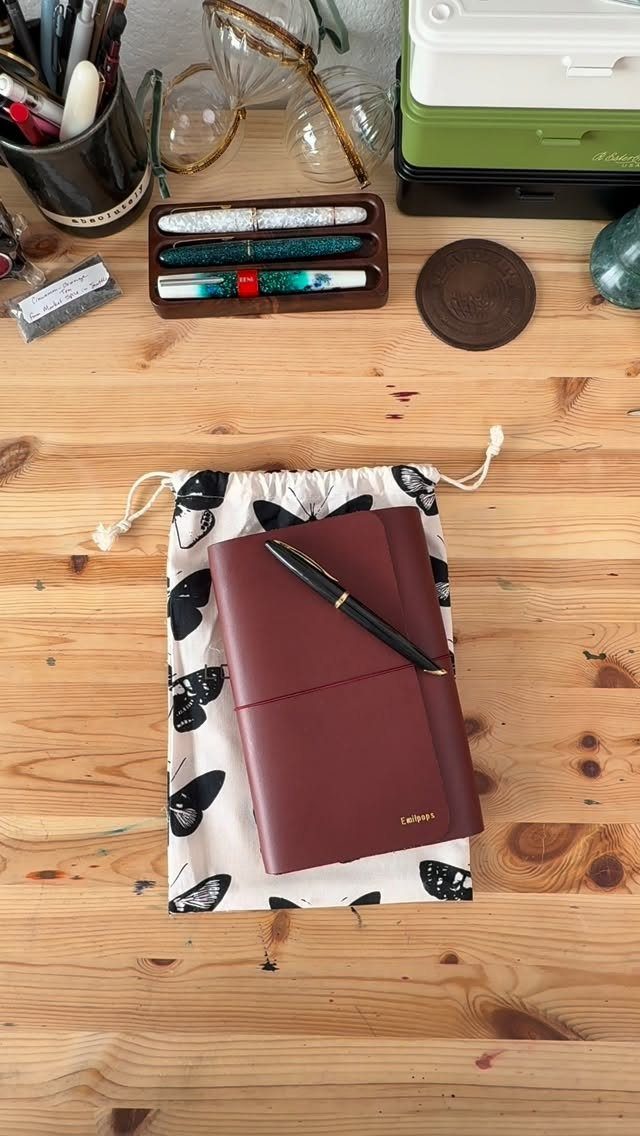 Burgundy leather journal and black pen on a butterfly print drawstring bag.
