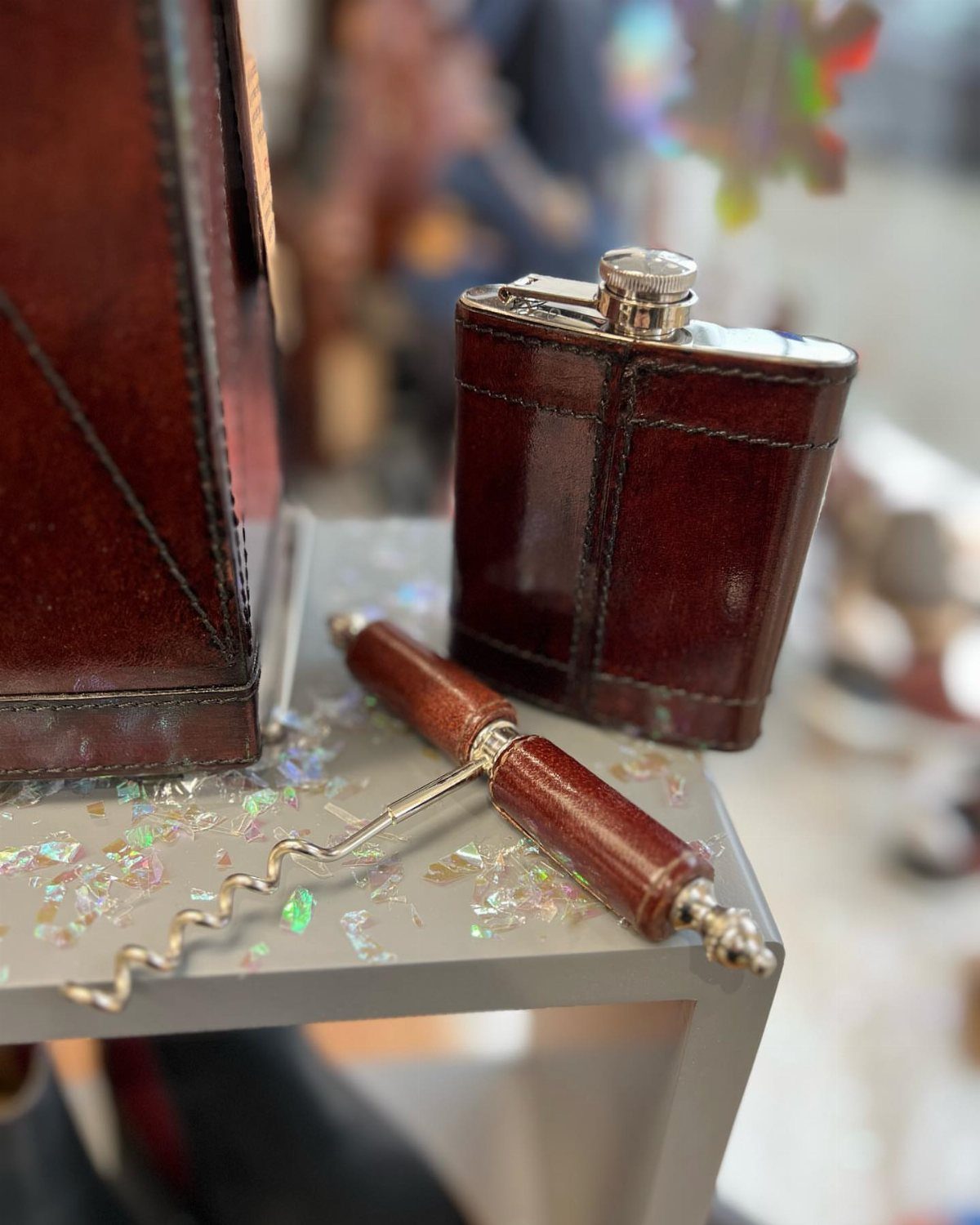 Leather-wrapped hip flask and corkscrew on a grey surface with iridescent confetti.