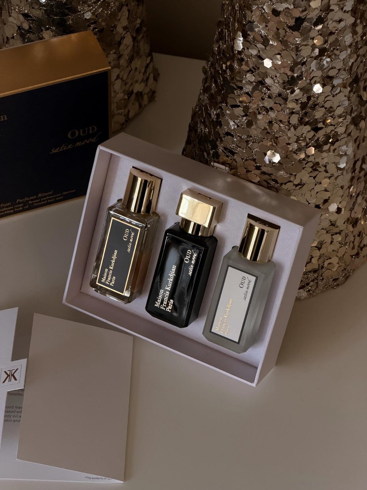 Three perfume bottles in a white gift box with gold glittery background decorations.