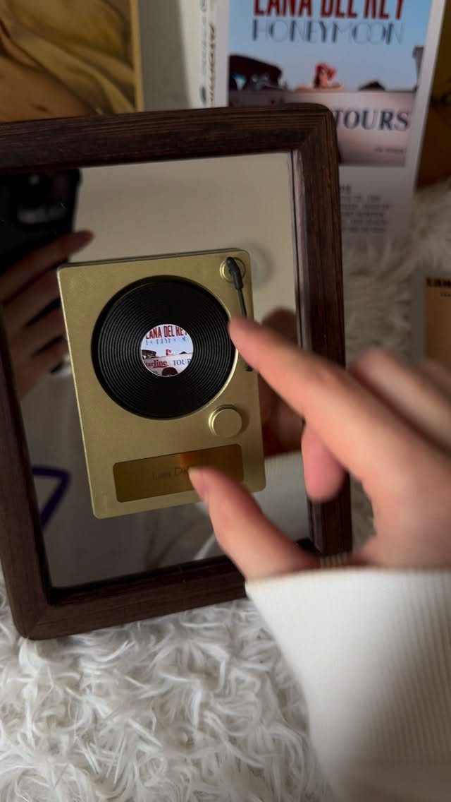 Small gold music player with miniature vinyl record held in front of mirror