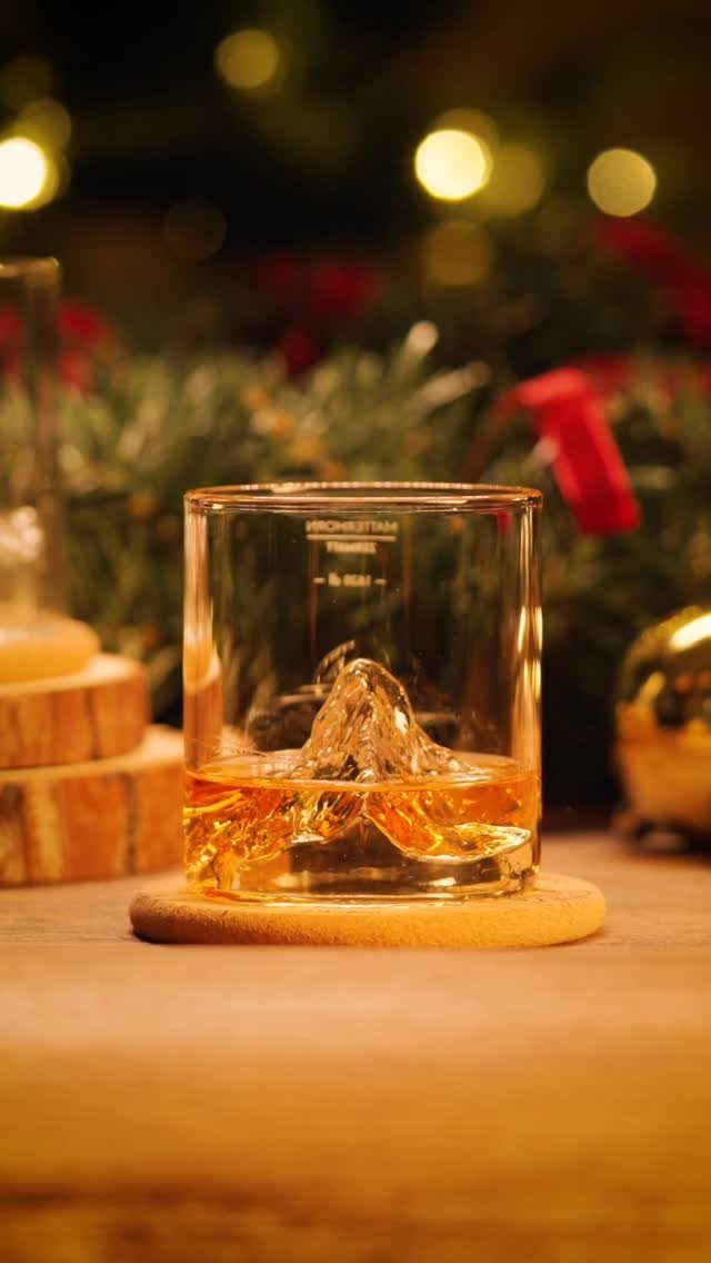Glass of whiskey with mountain ice cube on a wooden coaster, festive background