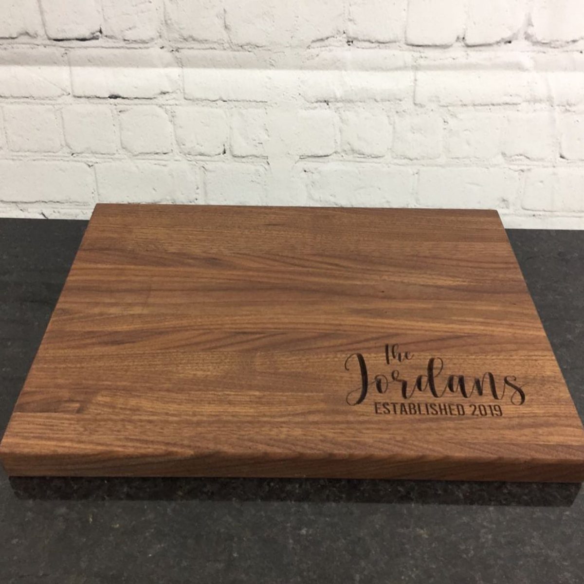 Wooden cutting board engraved with The Jordans Established 2019 on a dark counter