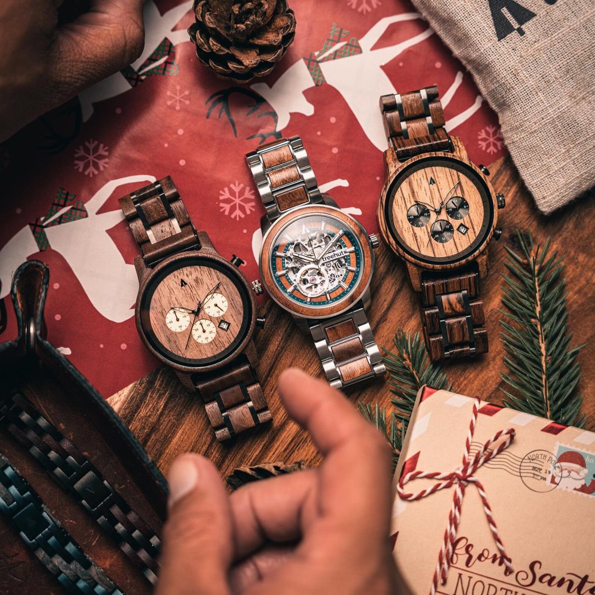 Three wooden wristwatches arranged on red Christmas wrapping paper with festive decorations.