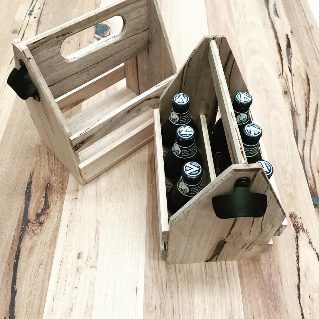 Wooden beer carriers on a table, one containing six brown glass beer bottles.