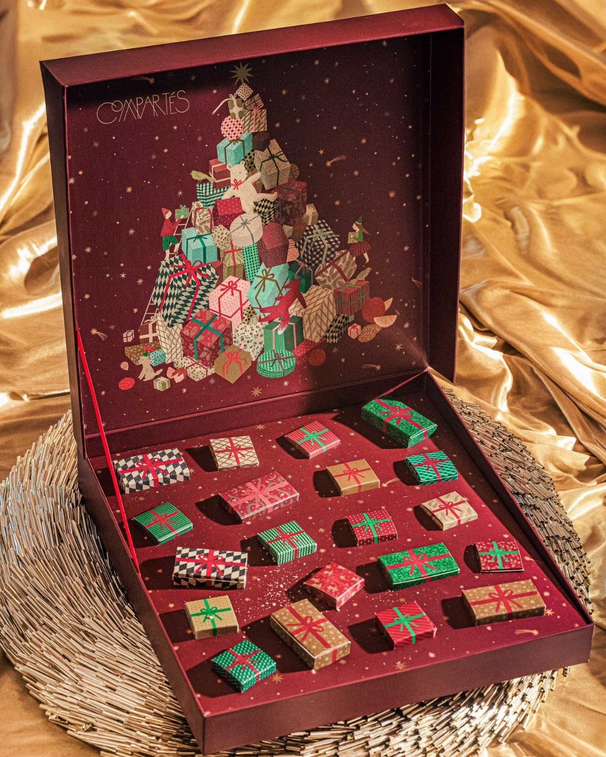 Open burgundy advent calendar box filled with small wrapped colorful Christmas presents.