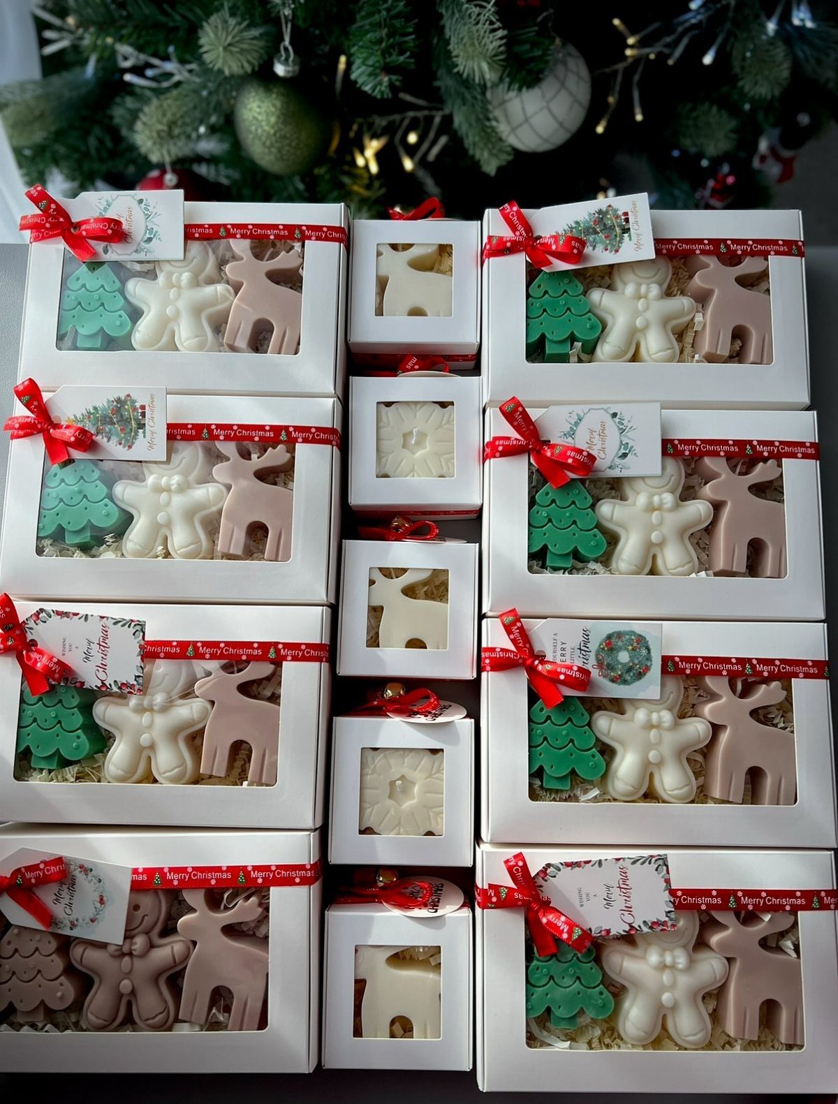 White gift boxes containing Christmas-shaped wax melts with red ribbons and tags.