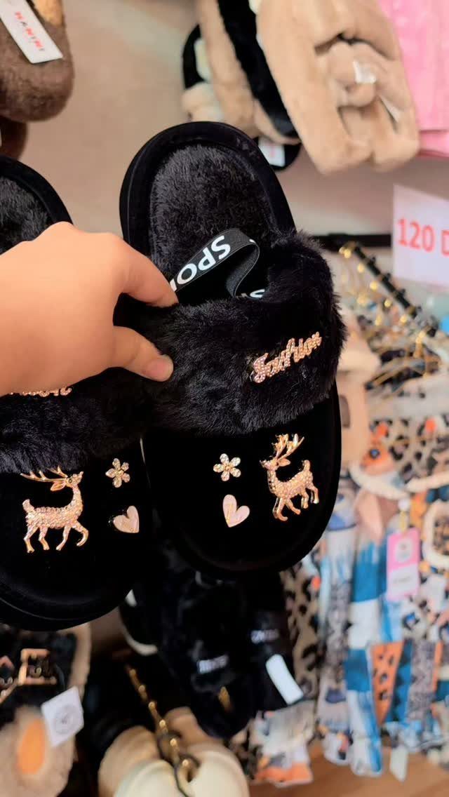 Black fluffy slippers with gold glittery deer and heart designs held by a hand.