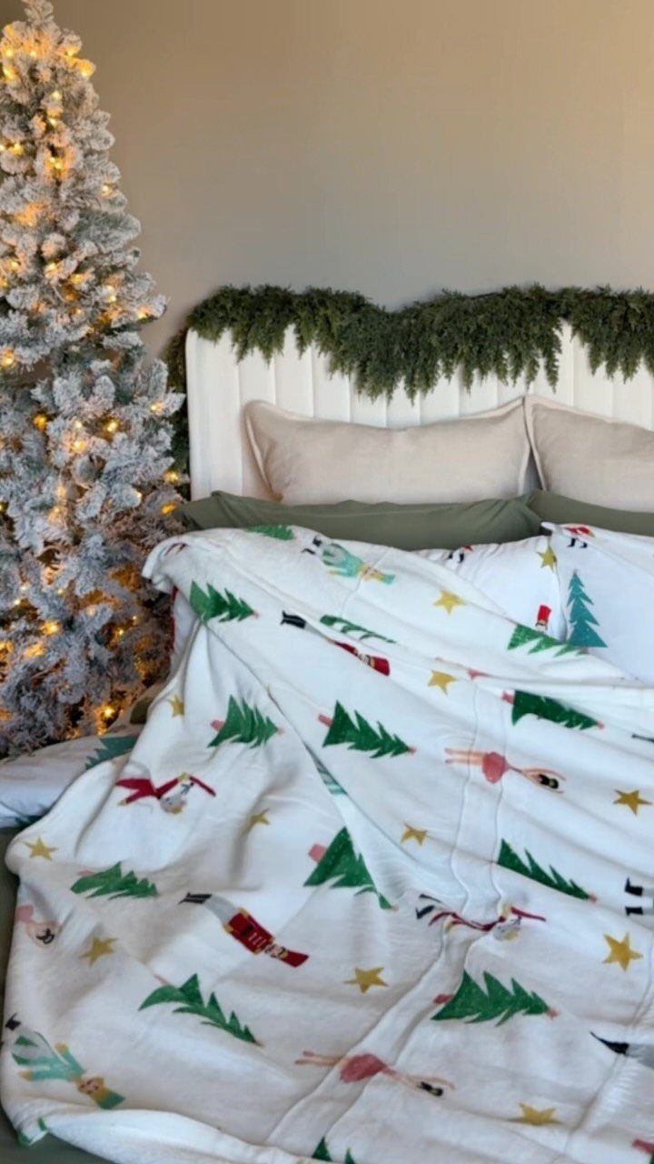Festive white Christmas print blanket draped over a bed next to a flocked tree