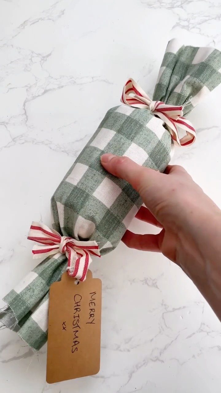 Hand holding a gift wrapped in green checkered fabric with a Christmas tag.